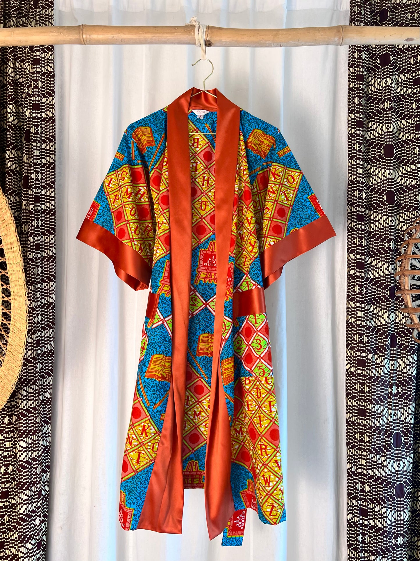 Colorful patterned garment hanging on a rack with a white curtain background