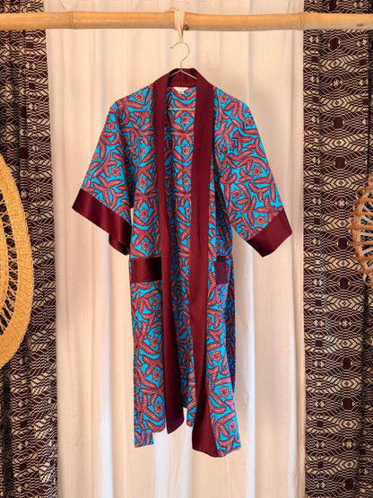 Burgundy and blue patterned robe hanging on a wooden stick against a white curtain with decorative elements.