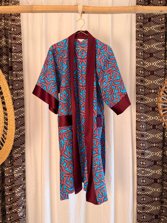 Burgundy and blue patterned robe hanging on a wooden stick against a white curtain with decorative elements.